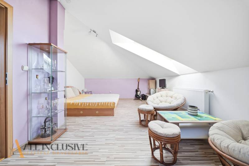 Podkrovní pokoj v rodinném domě s podlahou s dřevěným dekorem, nábytkem a střešními okny.