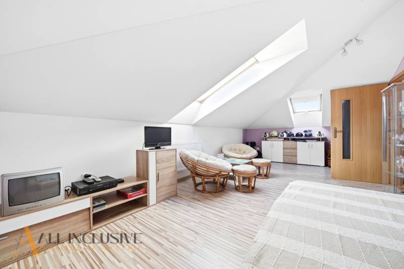 Podkrovní místnost v rodinném domě s křesly a podlahou s dřevěným dekorem.