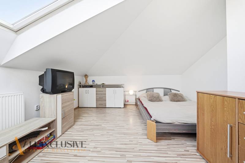 Podkrovní ložnice s televizí, postelí a skříněmi v rodinném domě.