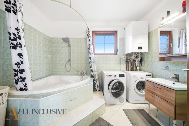 Koupelna s vanou, sprchou, pračkou a sušičkou v rodinném domě.