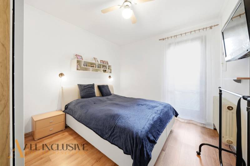 Ložnice v rodinném domě s postelí, dřevěným dekorem podlahy a televizorem na stěně.