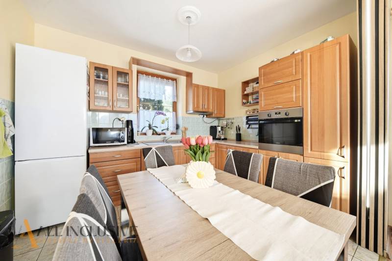 Kuchyně v rodinném domě s dřevěným dekorem nábytku a vybavením, květinová dekorace na stole.