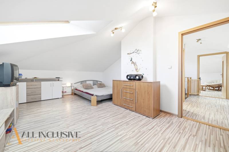 Světlá ložnice s podlahou s dřevěným dekorem, komodou a postelí v rodinném domě.