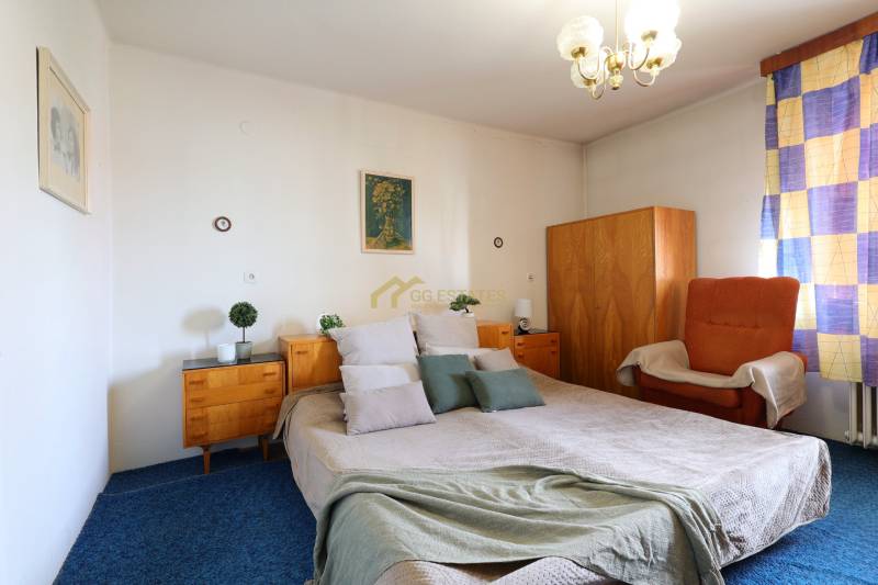 Ložnice s velkou postelí, dřevěnými skříňkami a křeslem v rodinném domě.