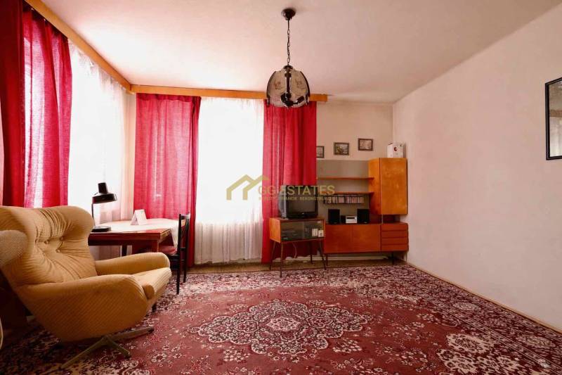 Obývací pokoj v rodinném domě s červeným kobercem, křeslem a závěsy na oknech.