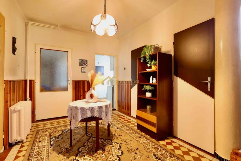 Interiér rodinného domu s kobercovou podlahou, v pozadí skříňka a osvětlení.