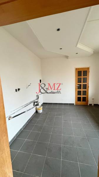 Prázdná místnost v 2-pokojovém bytě, podlaha z tmavé dlažby, bílé stěny, dřevěné dveře.