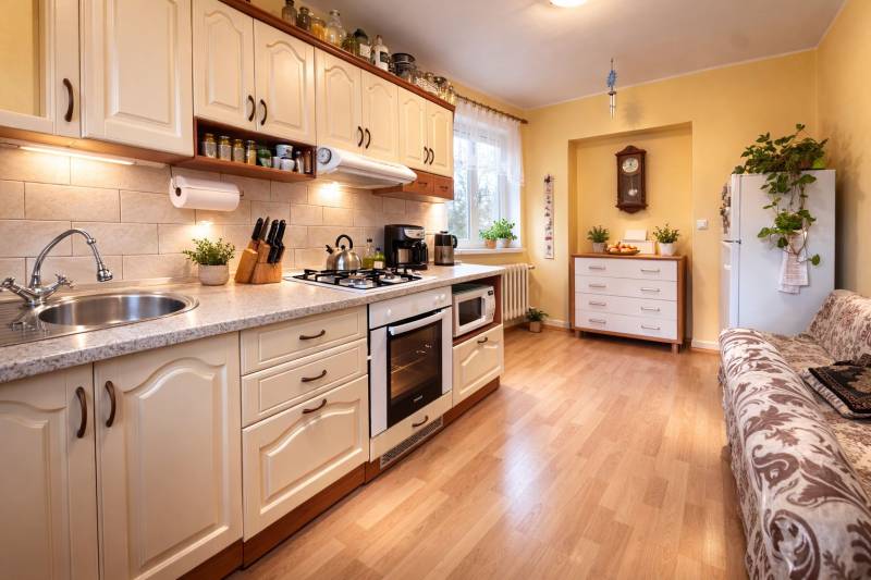 Kuchyně v 2-pokojovém bytě s podlahou s dřevěným dekorem, světlá linka a rostliny.