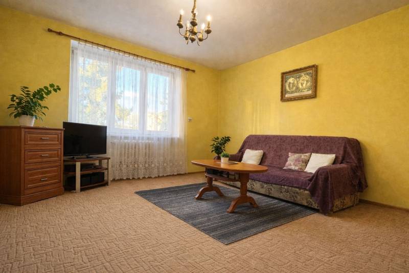 Obývací pokoj v dvoupokojovém bytě, se žlutými stěnami, kobercem a nábytkem.