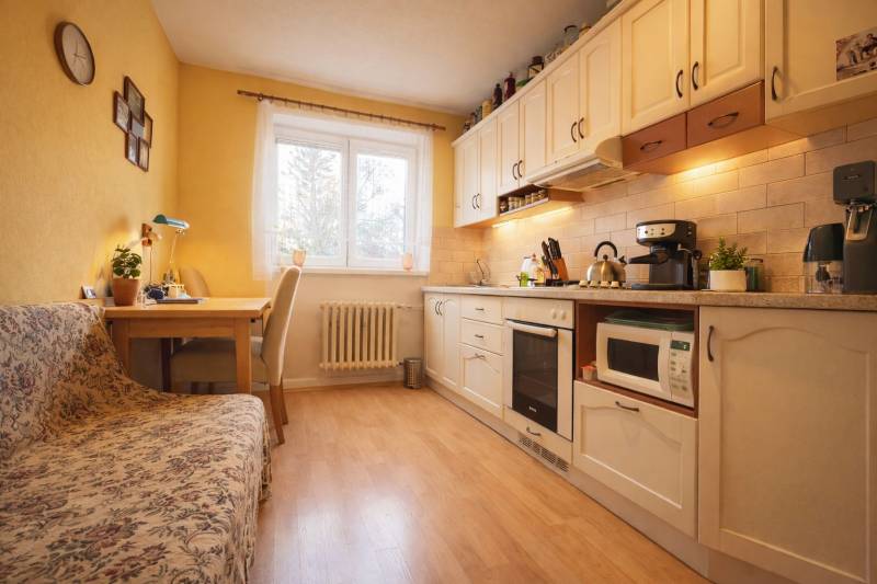 Kuchyně v 2-pokojovém bytě s dřevěným dekorem podlahy, světlým nábytkem a jídelním koutem.