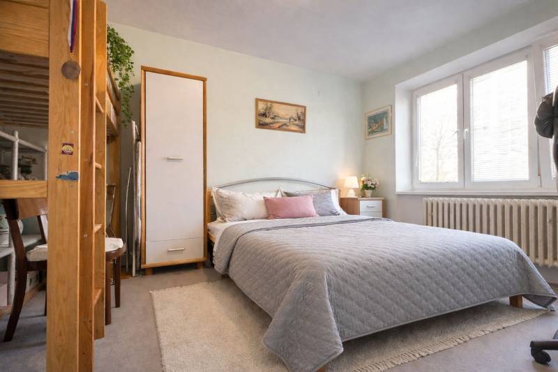 Ložnice v dvoupokojovém bytě s velkou postelí, dekoracemi a naturalistickým osvětlením.