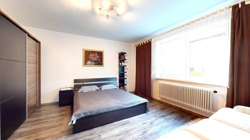 Ložnice v rodinném domě s postelí, skříňkou, obrazem a podlahou s dřevěným dekorem.