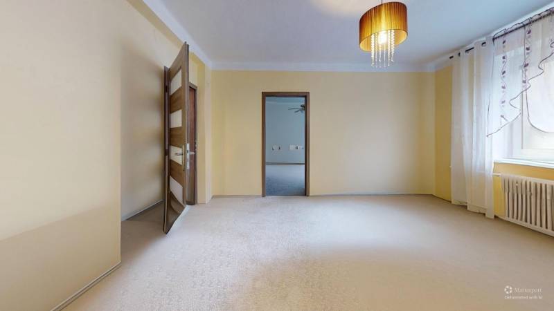 Světlý pokoj v rodinném domě se záclonami, lustrem a otevřenými dveřmi.