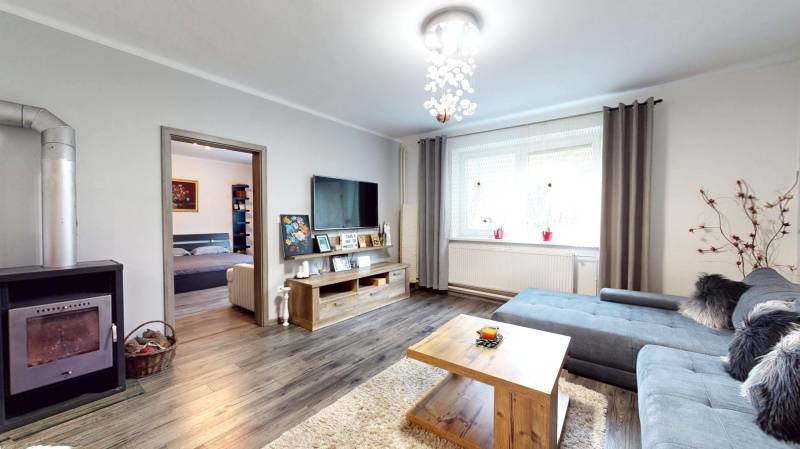 Obývací pokoj v rodinném domě s krbem, podlahou s dřevěným dekorem a sedací soupravou.