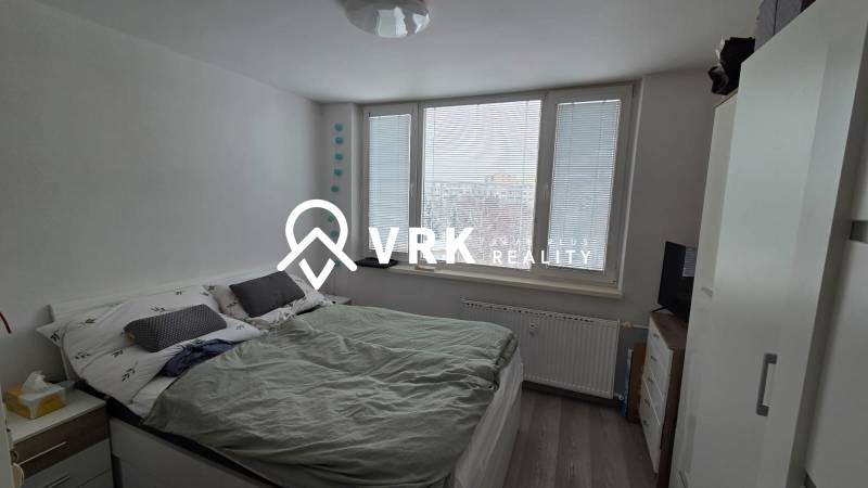 Ložnice s manželskou postelí, velkými okny a podlahou s dřevěným dekorem v třípokojovém bytě.