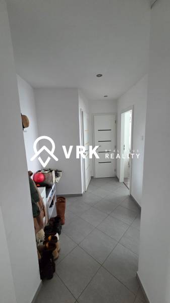 Chodba v 3-pokojovém bytě s šedou dlažbou, botník a boty na zemi.