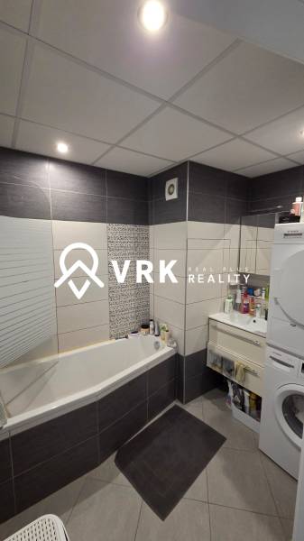 Koupelna v 3-pokojovém bytě s vanou, pračkou a tmavými obklady.