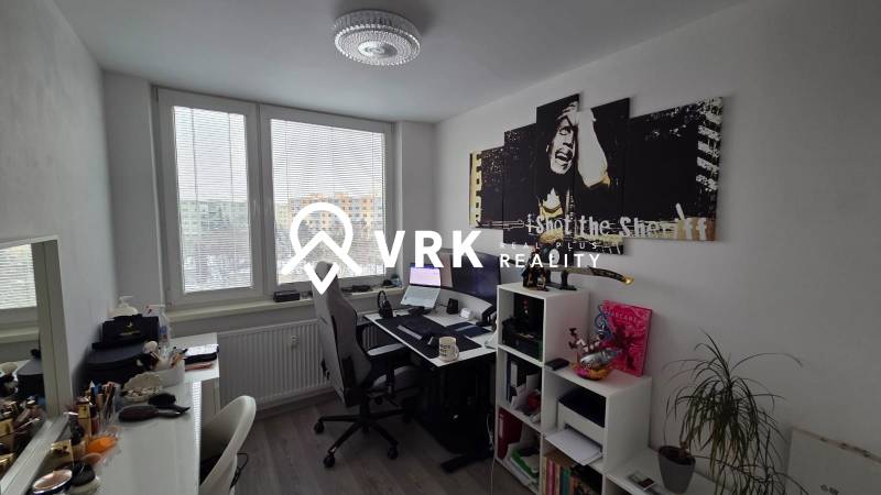 Pracovna ve 3-pokojovém bytě se stolem, regálem, obrazem a podlahou s dřevěným dekorem.