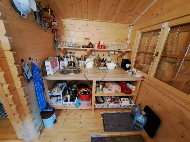 Dřevěná kuchyňka se spotřebiči, poličkami a dřezem v interiéru zahrad.