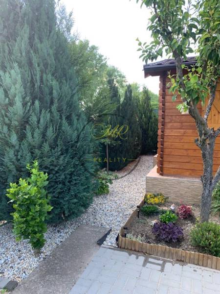 Zahrady v Dolních Krškanech, Nitra s upravenými jehličnany a dřevěným zahradním domkem.