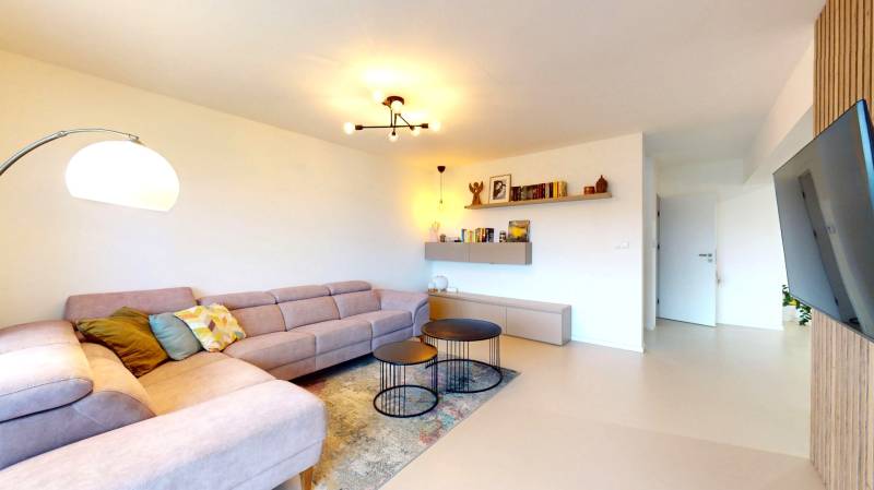 Obývací pokoj v rodinném domě s rohovou sedačkou, kulatými stolky a podlahou s dřevěným dekorem.