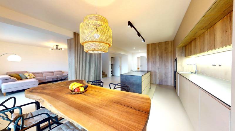 Kuchyně v rodinném domě s dřevěným stolem, pohovkou a moderním osvětlením.