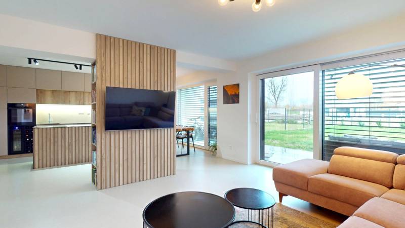 Obývací pokoj s velkými okny, pohodlnou sedačkou a dřevěným dekorem na stěně.