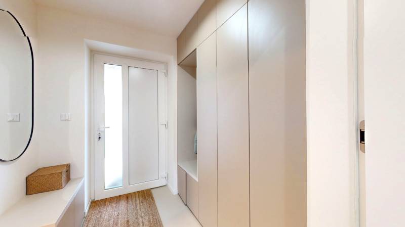 Vstupní chodba rodinného domu s věšákovou skříní, zrcadlem a kobercem.