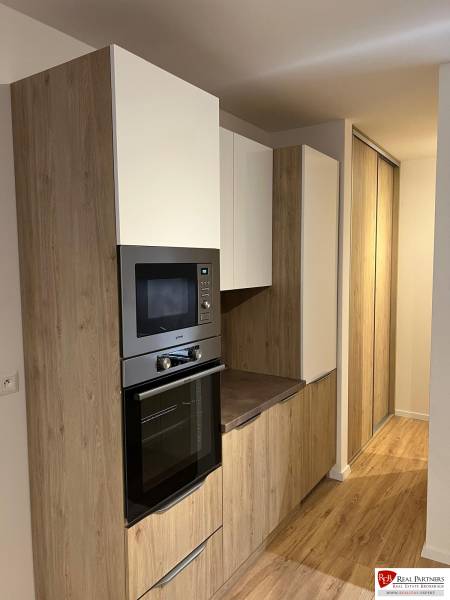 Kuchyňská část dvoupokojového bytu s podlahou s dřevěným dekorem a vestavěnými skříňkami.