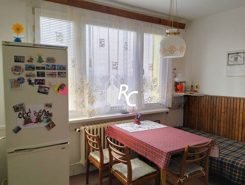 Kuchyně v 2-pokojovém bytě s jídelním stolem, židlemi a lednicí s magnetkami.