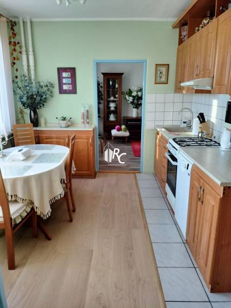 Kuchyň v 2pokojovém bytě s podlahou s dřevěným dekorem a stolem v rohu místnosti.