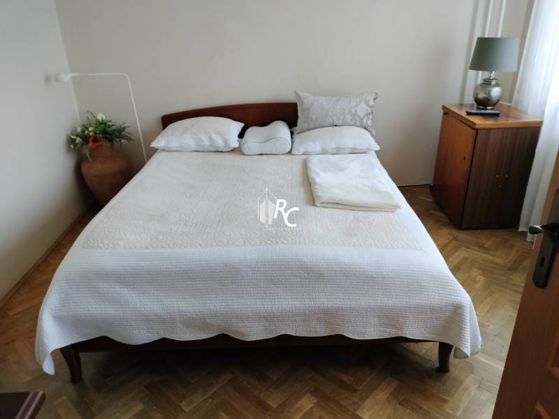 Ložnice s manželskou postelí, podlahou s dřevěným dekorem a nočním stolkem v 2-pokojovém bytě.