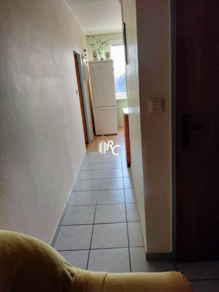 Chodba s ledničkou ve 2-pokojovém bytě, dlažba na podlaze, světlé stěny.