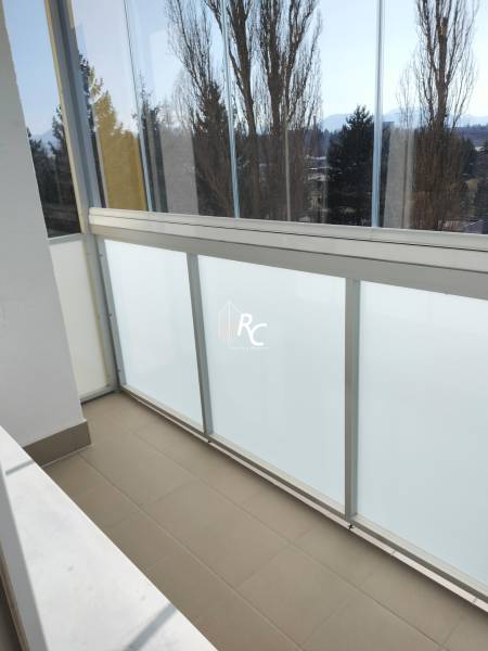 Zasklený balkon v 2-pokojovém bytě s výhledem na stromy a hory.