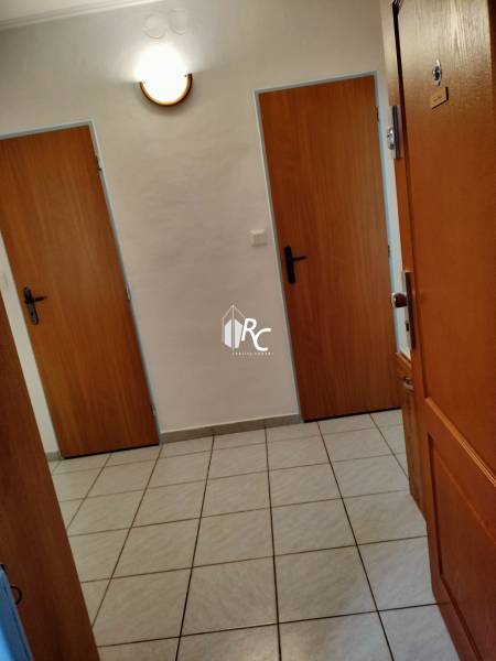 Vstupní chodba v 2pokojovém bytě s dlažbou a dřevěnými dveřmi.