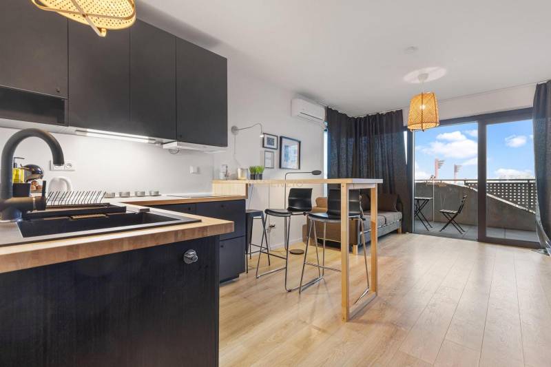 Kuchyně s černými skříňkami, barovým pultem a podlahou s dřevěným dekorem v 1-pokojovém bytě.