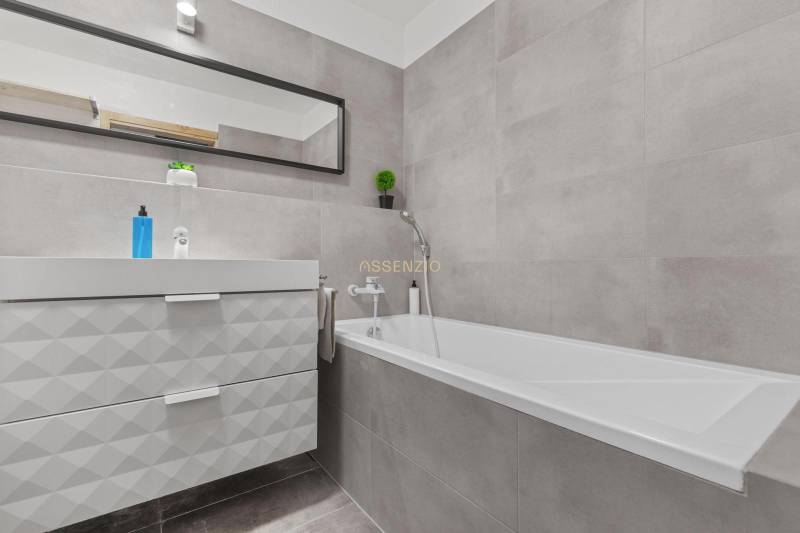 Koupelna s vanou, umyvadlem a zrcadlem v 1-pokojovém bytě.