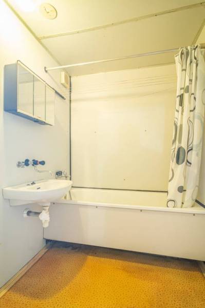 Koupelna s vanou a sprchovým závěsem v 2-pokojovém bytě, světlé stěny, oranžová podlaha.