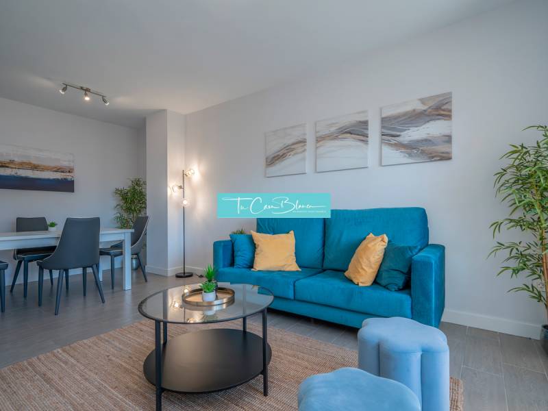 Obývací pokoj v 2-pokojovém bytě s modrou pohovkou a jídelním stolem.