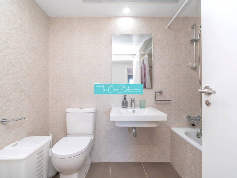 Koupelna v 2-pokojovém bytě s toaletou, umyvadlem, vanou a béžovým obkladem.