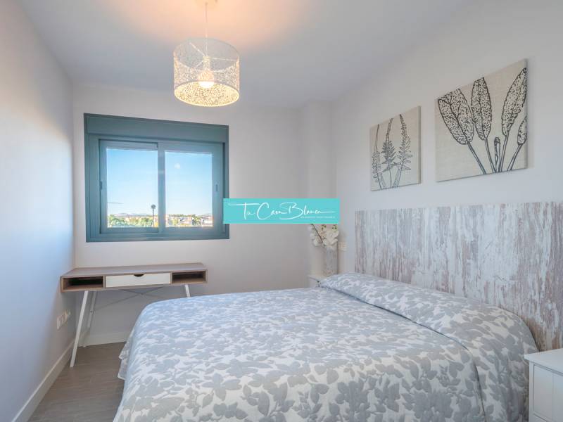 Ložnice v dvoupokojovém bytě se vzorovanou přikrývkou a dekoracemi na stěnách.