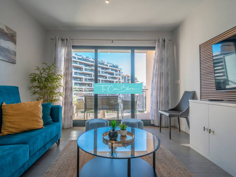 Obývací pokoj v 2-pokojovém bytě s terasou, modrou pohovkou a rostlinou.