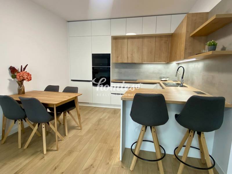 Kuchyně v 2-pokojovém bytě s podlahou s dřevěným dekorem, jídelním stolem a barovým pultem.