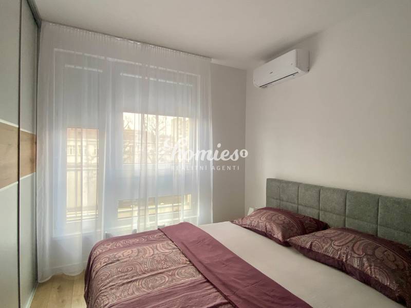 Ložnice v 2pokojovém bytě s klimatizací a podlahou s dřevěným dekorem.