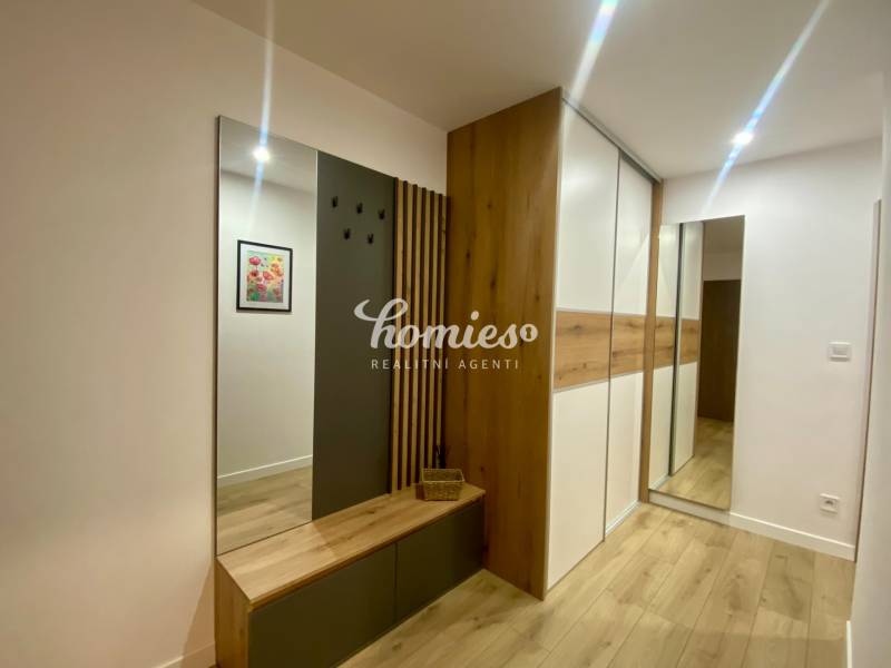 Interiér 2-pokojového bytu s podlahou s dřevěným dekorem, věšákovou stěnou a zrcadlem.