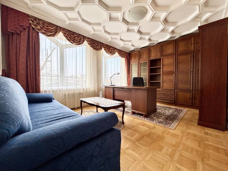 Pokoj ve 4pokojovém bytě s pohodlnou pohovkou, pracovním stolem a podlahou s dřevěným dekorem.