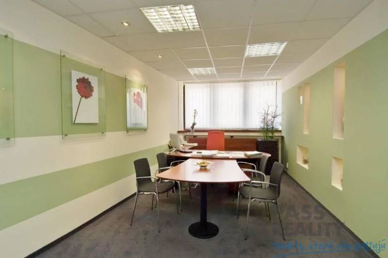 Kanceláře s pracovním stolem, židlemi, umístěné dekorace na stěnách a okno s vertikálními žaluziemi.