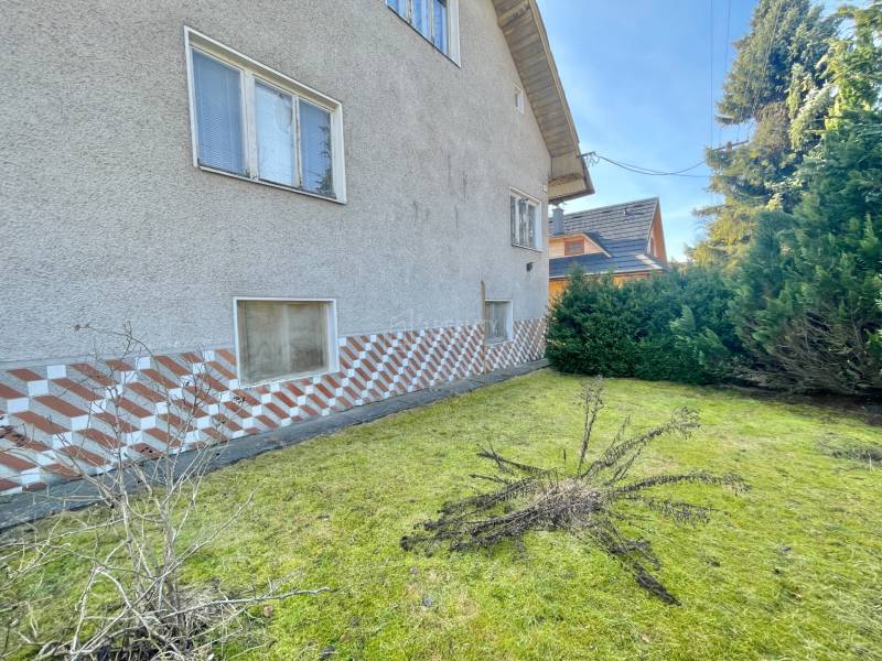 Rodinný dům v Terchové s travnatým pozemkem, obklopený keři a dekorativním obkladem.