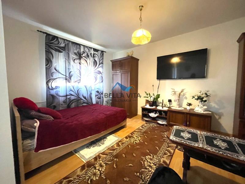 Pokoj s jednou postelí, televizí a podlahou s dřevěným dekorem.