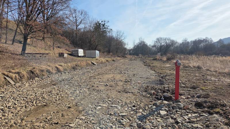 Pozemky - bydlení v Hanisce, kamenitá cesta mezi stromy a kontejner.